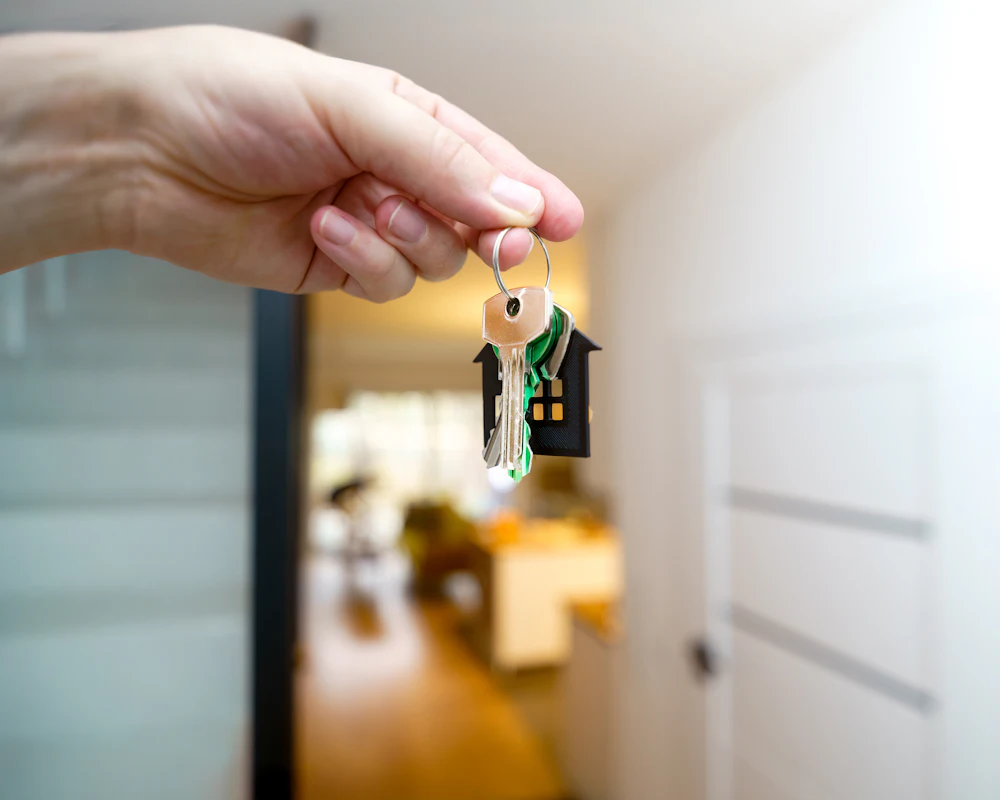 Main tenant les clés d’une maison devant la porte d’entrée ouverte